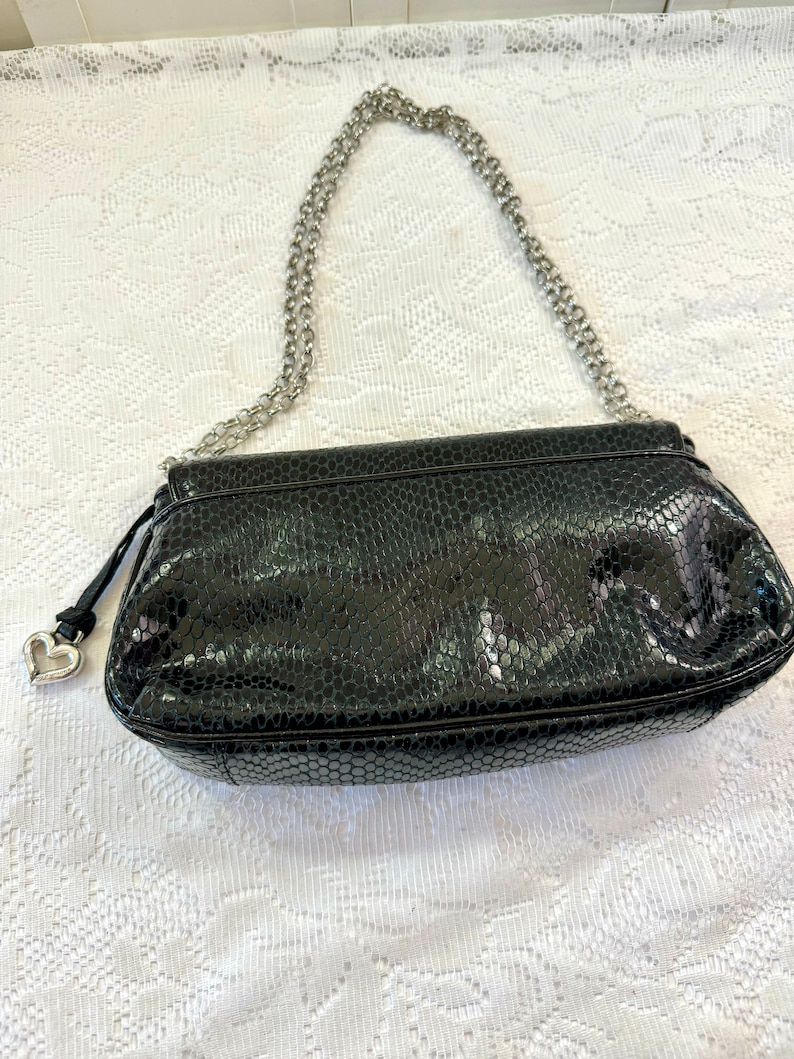 Op de afbeelding: Zwarte handtas van imitatieleer met een zilveren kettingriem en een hartvormige hanger.