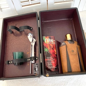 May include: A brown leatherette travel bar set with a silver bottle opener, a silver jigger, a green shot glass, and a brown leatherette flask with a gold top. The set is open and the inside is lined with burgundy fabric. The set includes a small booklet titled "Nite- Happy Hour" with recipes for drinks.