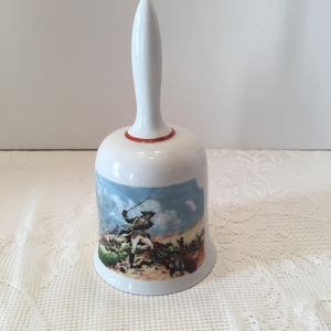 May include: White porcelain bell with a red rim and a painted image of a soldier on horseback. The soldier is holding a sword and is riding through a field.