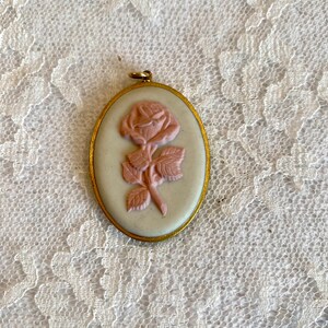 May include: Oval shaped pendant with a gold frame and a white cameo featuring a pink rose.