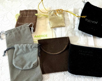 May include: Assortment of small, drawstring fabric bags in various colors and materials. The bags are labeled with the names of different brands, including "Ross-Simons", "AMIRCE", "REVV", and "GUERLAIN EMPORIUM".