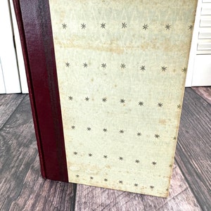 May include: A vintage hardcover book with a white cover and a burgundy spine. The cover has a repeating pattern of small stars.