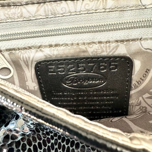 Op de afbeelding: Close-up van de binnenkant van een zilveren metallic tas met een zwart lederen label waarop "Fossil" en "E525765" staat. De voering van de tas heeft een bloemenpatroon.