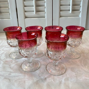 May include: Set of six clear glass stemmed drinking glasses with a ruby red rim. The glasses have a textured pattern and are perfect for serving cocktails or wine.