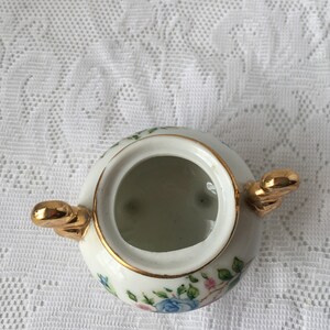 May include: White porcelain sugar bowl with a gold rim and floral design. The bowl has two gold handles and a lid.