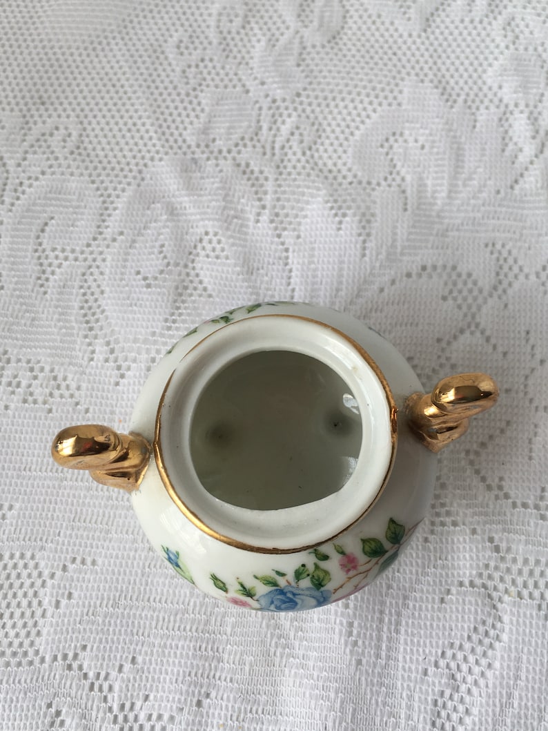 May include: White porcelain sugar bowl with a gold rim and floral design. The bowl has two gold handles and a lid.