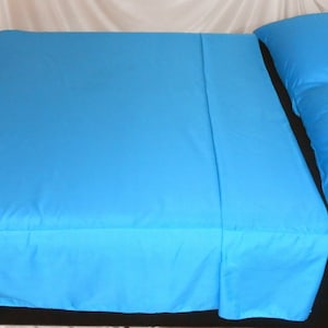 May include: A bright turquoise bed set, including a fitted sheet, flat sheet, and pillow. The sheets are neatly arranged on a bed, showcasing a smooth, solid color. The pillow is positioned on the right side of the bed, complementing the overall bedding ensemble.