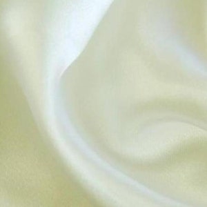 Puede incluir: Una tela lisa de color amarillo pálido con un brillo sutil. La tela está drapeada y doblada, creando curvas y pliegues suaves.