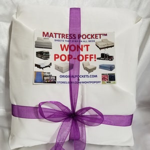 Peut inclure: Un sac cadeau blanc avec un ruban violet noué en forme de nœud. Le sac porte une étiquette qui dit "Mattress Pocket™ Sheets that stay on all beds Won't Pop-Off!" avec des images de différents types de lits. L'étiquette comprend également l'adresse du site Web "ORIGINALPOCKETS.COM & STORES.EBAY.COM/WONTPOPOFF".
