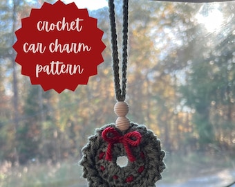 May include: A crocheted wreath car charm with a red bow hanging from the rearview mirror of a car. The wreath is green and has red accents. The charm is hanging from a brown cord.