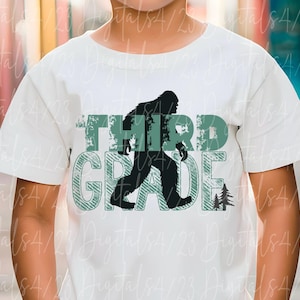 May include: White t-shirt with a green and black graphic. The graphic features the words "THIRD GRADE" with a silhouette of a Bigfoot walking. A small tree graphic is next to the word "GRADE".
