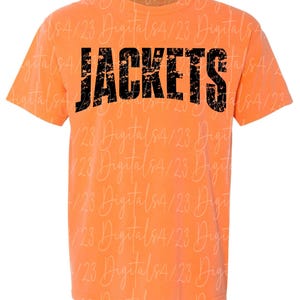 Puede incluir: Camiseta naranja con la palabra "JACKETS" impresa en letras negras desgastadas. La camiseta tiene mangas cortas y cuello redondo. Prenda casual.