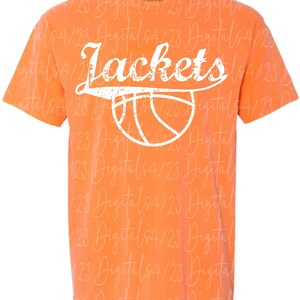 May include: Orange t-shirt featuring the word "Jackets" in white script above a white basketball graphic. The shirt has a crew neck and short sleeves. The text and graphic have a distressed effect.