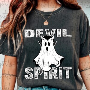 May include: Dark gray t-shirt with the words "DEVIL SPIRIT" in distressed white lettering. A white ghost-like figure with devil horns and a black face is centered between the words. The shirt is a casual style.