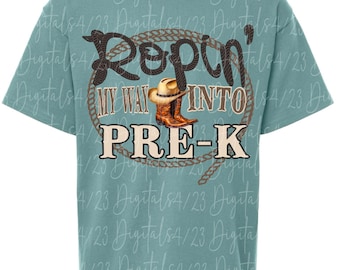 May include: A turquoise t-shirt with a graphic design featuring the text "Ropin' My Way Into Pre-K". The design includes a rope circle, cowboy boots, and a cowboy hat.