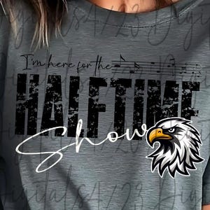 May include: Gray t-shirt with the text "I'm here for the HALFTIME SHOW" in black, with musical notes above the word "HALFTIME" and an eagle graphic. The eagle has a yellow beak and is in black and white.
