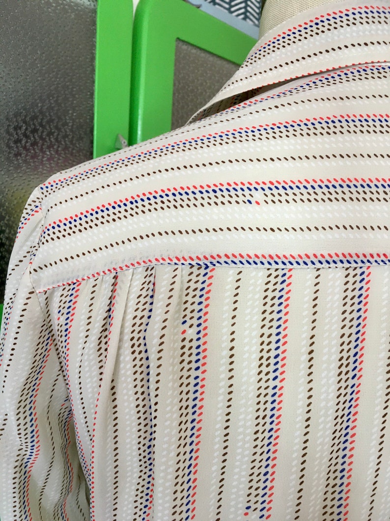Op de afbeelding: Een wit overhemd met knopen en bruine, blauwe en rode strepen. Het shirt heeft een gestippeld patroon op de strepen.