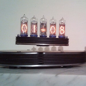 Puede incluir: Un reloj digital único con números naranjas brillantes mostrados en tubos de vacío. El reloj presenta una base de madera en capas y un controlador de energía separado con luces indicadoras. La hora mostrada es 01:08.