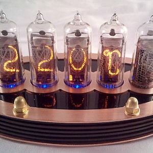 Puede incluir: Un reloj de color cobre con cuatro tubos Nixie que muestran la hora "2201". El reloj tiene una base negra con un borde de color cobre.