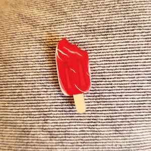 Peut inclure: Une sucette rouge avec une morsure, sur un bâton, sur un fond texturé.