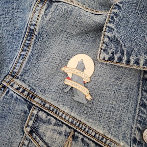May include: A blue denim jacket with a gray wolf howling at the moon enamel pin. The pin has a white banner with the text "Werewolves Not Swimwear" in black.