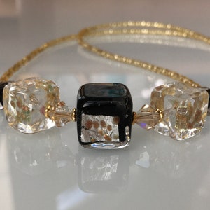 May include: A gold chain necklace with three square glass beads. The center bead is black with gold flecks, and the two outer beads are clear with gold flecks.
