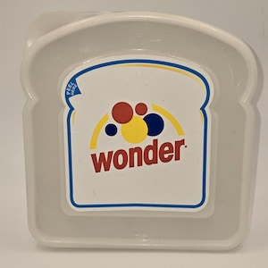 May include: A clear, plastic sandwich container shaped like a slice of bread. The container features a white label with the word "wonder" in red, and a colorful design of red, yellow, and blue circles. The label is outlined in blue.
