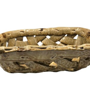 May include: A rectangular ceramic basket with a glossy, light tan glaze and a woven lattice design. The rim features a textured, uneven edge with darker brown accents, creating a handcrafted appearance with open spaces between the ceramic strips.