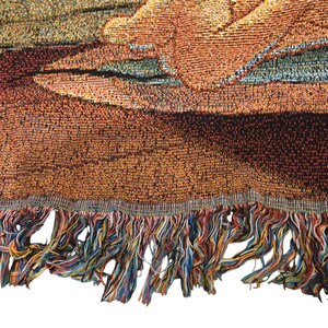 May include: A woven tapestry blanket featuring a textured, multi-colored design with warm tones of orange, brown, and gold. The fabric displays a detailed, intricate pattern and is finished with a decorative, multi-colored fringe along the bottom edge.