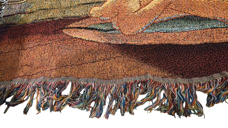 May include: A woven tapestry blanket featuring a textured, multi-colored design with warm tones of orange, brown, and gold. The fabric displays a detailed, intricate pattern and is finished with a decorative, multi-colored fringe along the bottom edge.