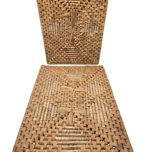 May include: Two rectangular woven placemats made from natural tan fibers. Each mat features a complex, repeating geometric pattern created by varying the weave density and direction of the dried plant material, resulting in a textured surface.