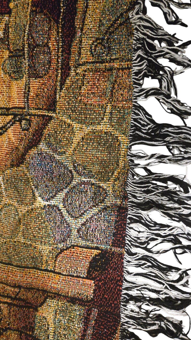 May include: A woven tapestry throw blanket featuring a complex pattern of interlocking geometric shapes in shades of gold, brown, and deep red. The fabric has a textured finish and is finished with a long, frayed fringe edge in black and white.