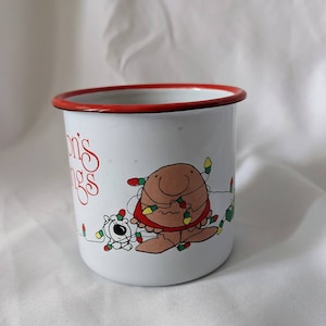 May include: White enamel mug with a red rim. It features a cartoon illustration of a person with a dog, both tangled in Christmas lights. The text "Jon's Greetings" is printed on the mug.