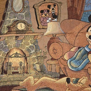 May include: A woven tapestry featuring a cozy indoor scene with a stone fireplace, a mantel clock, and a framed portrait of two cartoon characters. A lamp sits on a side table next to an armchair, while a yellow dog rests on a rug in the foreground.