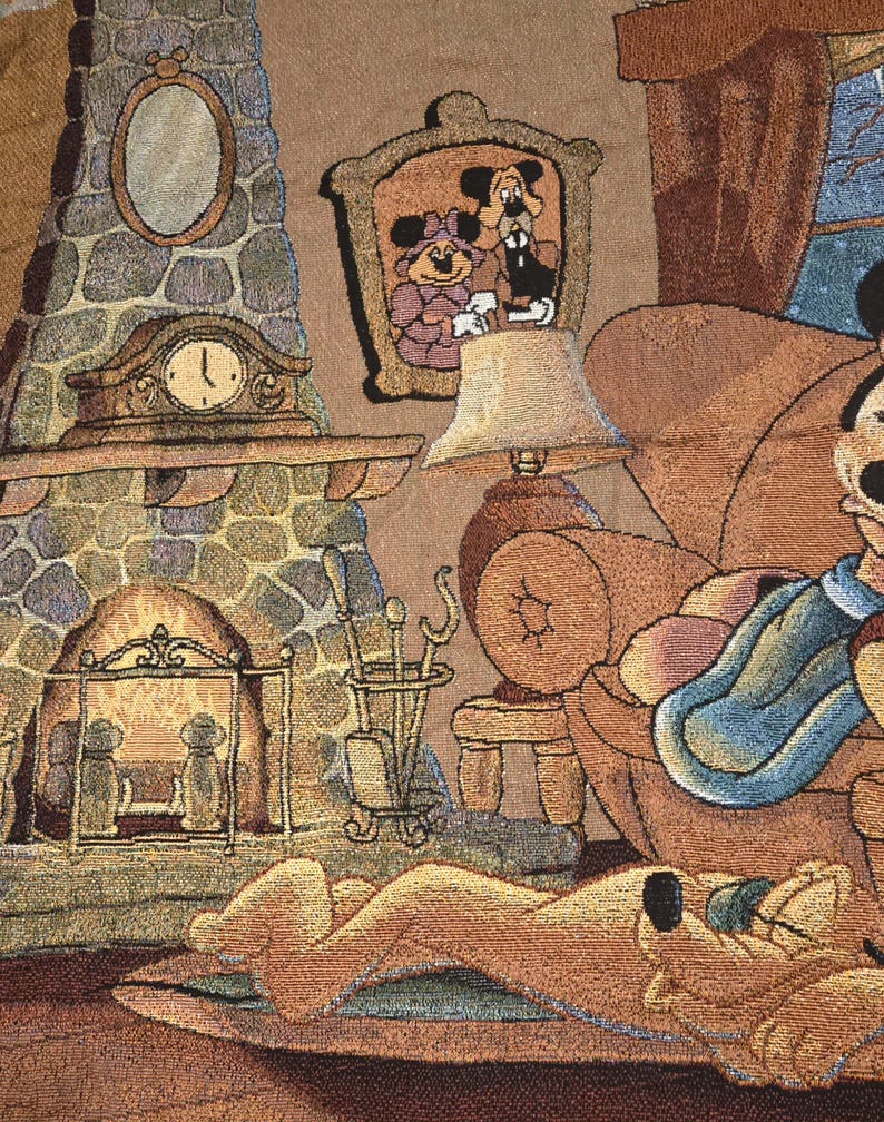 May include: A woven tapestry featuring a cozy indoor scene with a stone fireplace, a mantel clock, and a framed portrait of two cartoon characters. A lamp sits on a side table next to an armchair, while a yellow dog rests on a rug in the foreground.