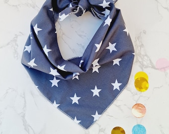 May include: A dark blue bandana with white stars printed on it. The bandana is folded in a triangular shape and is ready to be tied around a pet's neck.