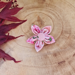 May include: A pink fabric flower hair clip with a floral pattern and a pink button center.