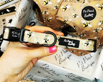 May include: A beige dog collar with a black buckle and a black label that says "Pet Pooch Boutique". The collar has a bee pattern with yellow and black bees on a beige background.