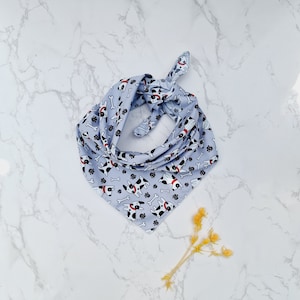May include: A light blue bandana with a white background and a pattern of black and white dogs with red collars and white bones.