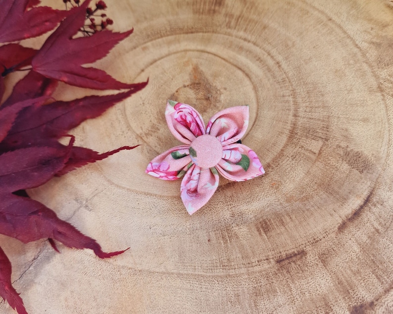 May include: A pink fabric flower hair clip with a floral pattern and a pink button center.