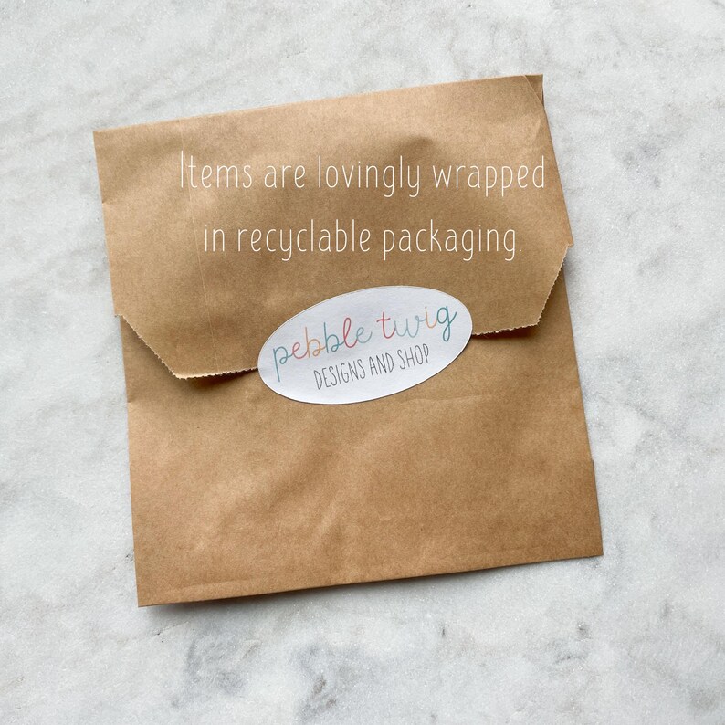Pu&ograve; includere: Un pacco di carta marrone con il testo "Items are lovingly wrapped in recyclable packaging." e un adesivo che dice "pebble twig DESIGNS AND SHOP".