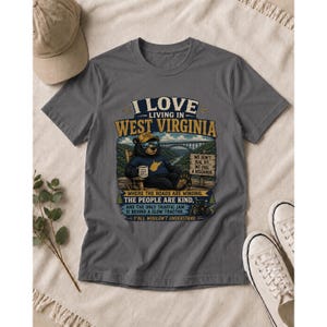 Puede incluir: Una camiseta gris carb&oacute;n con un gr&aacute;fico de un oso con gafas de sol y gorra, sentado en una silla con una taza. El texto dice: I LOVE LIVING IN WEST VIRGINIA, WHERE THE ROADS ARE WINDING, THE PEOPLE ARE KIND, AND THE ONLY TRAFFIC JAM IS BEHIND A SLOW TRACTOR. Y'ALL WOULDN'T UNDERSTAND.