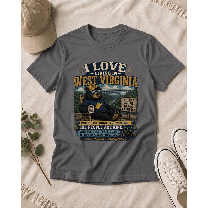 Puede incluir: Una camiseta gris carb&oacute;n con un gr&aacute;fico de un oso con gafas de sol y gorra, sentado en una silla con una taza. El texto dice: I LOVE LIVING IN WEST VIRGINIA, WHERE THE ROADS ARE WINDING, THE PEOPLE ARE KIND, AND THE ONLY TRAFFIC JAM IS BEHIND A SLOW TRACTOR. Y'ALL WOULDN'T UNDERSTAND.