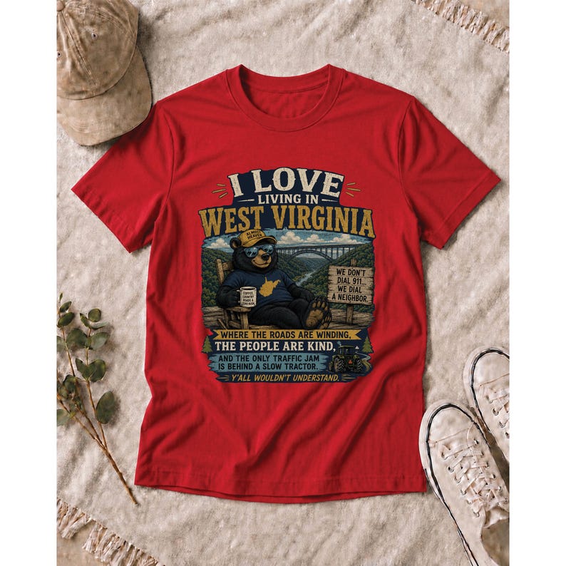 Puede incluir: Una camiseta roja de manga corta con el gr&aacute;fico de un oso con gafas de sol y sombrero, sentado en una silla. El texto dice I LOVE LIVING IN WEST VIRGINIA, WHERE THE ROADS ARE WINDING, THE PEOPLE ARE KIND, AND THE ONLY TRAFFIC JAM IS BEHIND A SLOW TRACTOR. Y'ALL WOULDN'T UNDERSTAND.