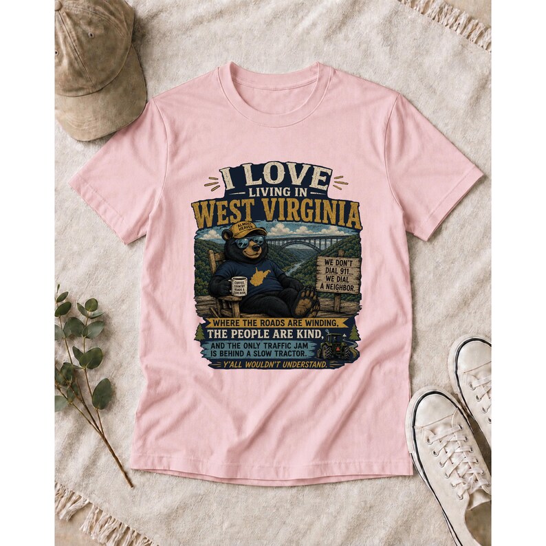Puede incluir: Una camiseta rosa claro con el gr&aacute;fico de un oso con gafas de sol y sombrero, sentado en una silla con una taza. El texto dice I LOVE LIVING IN WEST VIRGINIA, WE DON'T DIAL 911, WE DIAL A NEIGHBOR, WHERE THE ROADS ARE KIND, Y'ALL WOULDN'T UNDERSTAND.