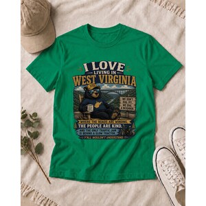 Puede incluir: Una camiseta verde de manga corta con un gr&aacute;fico de un oso sentado en una silla y el texto I LOVE LIVING IN WEST VIRGINIA, WE DON'T DIAL 911, WE DIAL A NEIGHBOR, WHERE THE ROADS ARE WINDING, THE PEOPLE ARE KIND, Y Y'ALL WOULDN'T UNDERSTAND.