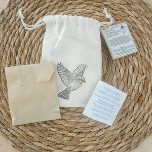 May include: A cream-colored drawstring pouch featuring a black line-art illustration of a bird in flight. The pouch includes a tag labeled Native Northeast Seed Mix, a small brown paper envelope, and a white informational card with printed text.