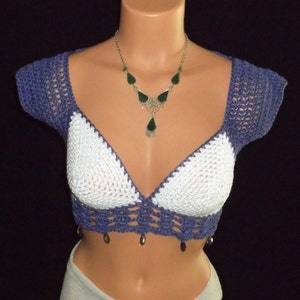 May include: A white and purple crocheted crop top with a beaded trim. The top has a deep V-neckline and short sleeves.