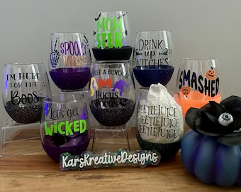 May include: A collection of stemless wine glasses with Halloween-themed designs. Each glass features glitter at the base and various phrases like "Spooky Vibes" and "I'm Here for the Boos". The glasses are decorated with Halloween-related graphics.