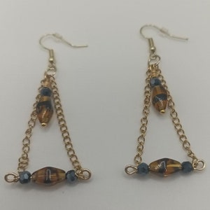 May include: A pair of gold dangle earrings with brown and black glass beads and dark blue beads. The earrings have a triangular shape.
